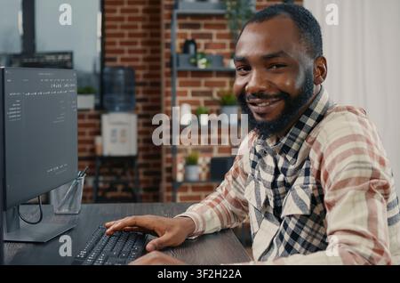 Software developer types programming code on a computer keyboard, turning with a confident smile while working on online cloud computing in an office. Stock Photo