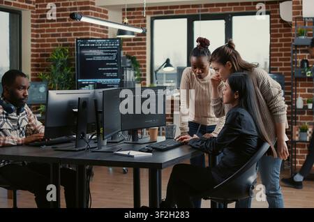 Diverse engineers brainstorm software code library while a developer team discusses algorithms, database work and new software ideas across office computer screens. Stock Photo