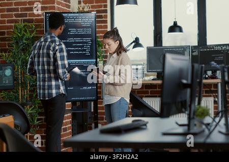 Developer presents code errors with tablet as engineers use a tablet and wall display to review bugs, cloud computing and team software development in an IT office. Stock Photo