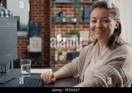 Smiling engineer types source code at a desk in a development agency, combining programming language, laptop coding and a confident technology portrait. Stock Photo