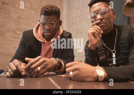 To hesitate together, two men deep in conversation inside, focused expressions with glasses and rings, broody moody, deep talk, regret, regretting som Stock Photo