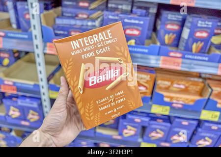 Integral whole wheat penen rigate, pack of Barilla whole grain penne rigate held in hand in front of a supermarket shelf, pack of noodles, supermarket Stock Photo
