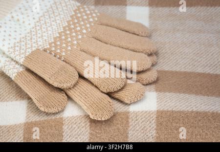 Beige knitted gloves on a plaid fabric background Stock Photo