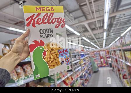 Large Mega Kellogg's corn flakes pack in the supermarket, held by one hand, food product, cereal breakfast food product packaged, grocery store, buy p Stock Photo