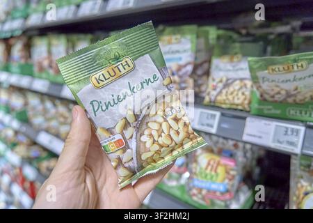 Round pack of pine nuts from Kluth on supermarket shelf, held by one hand, shopping for product, Sussermarkt Laden, Rewe, Germany Stock Photo