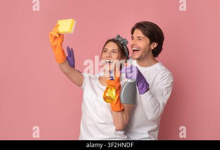 Cleaning Selfie. Joyful young couple using sponge like smartphone, fooling together Stock Photo