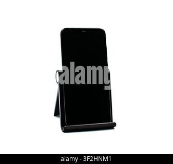 A modern black smartphone with a blank screen, positioned vertically on an adjustable desktop stand, isolated on a white background Stock Photo