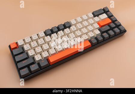 A wireless mechanical computer keyboard with grey, white, and bright orange keycaps lies on a smooth beige background. Stock Photo