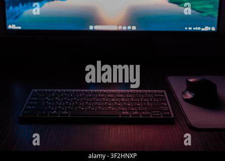 Workstation setup featuring a computer mouse, keyboard, and glowing monitor screen in dim lighting. Stock Photo