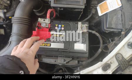 Mechanic hand touching red terminal on car battery under hood Stock Photo