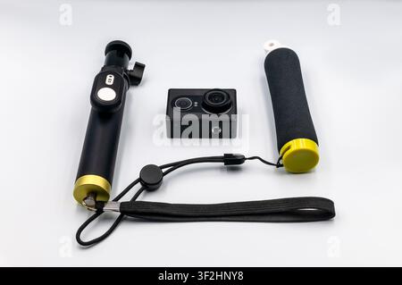 A black action camera surrounded by accessories including a selfie stick with a remote control and a floating hand grip on a seamless white background Stock Photo