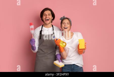Cheerful Millennial Couple With Cleaning Supplies In Hands Over Pink Background Stock Photo