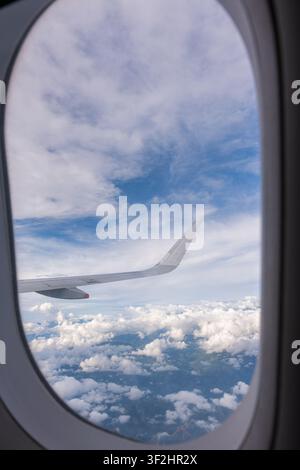 Airplane wing extends over a tranquil expanse of clouds and blue sky, viewed from a passenger window, illustrating concepts of travel, journey, freedo Stock Photo