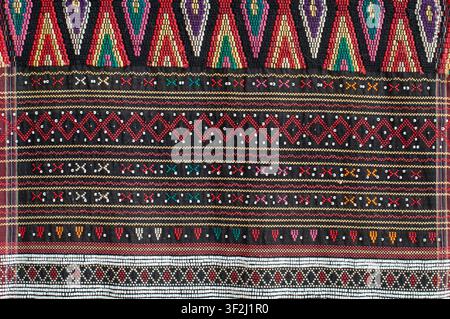 Detailed view of colorful Indonesian Batak Ulos textile showcasing geometric tribal patterns, bead embroidery, and traditional weaving on dark fabric. Stock Photo