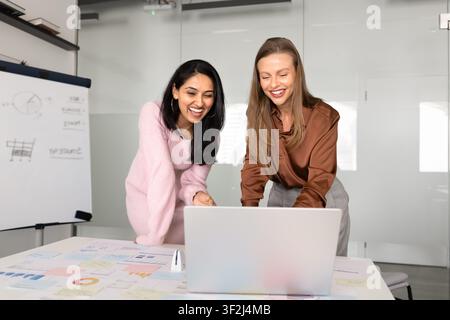 Smiling colleagues reviewing project data on laptop in corporate office Stock Photo