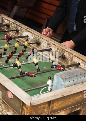 Vintage foosball table, worn wood frame. Players in yellow and red uniforms. Two hands poised, ready to engage. Casual, competitive atmosphere. Perfec Stock Photo