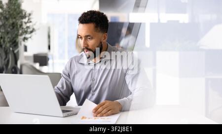 Focused businessman working on report seated at desk with laptop Stock Photo