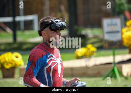 Kyiv, Ukraine - July 17, 2026: A man wearing FPV video goggles operates a racing drone with a remote controller during an outdoor event at VDNH (Expoc Stock Photo