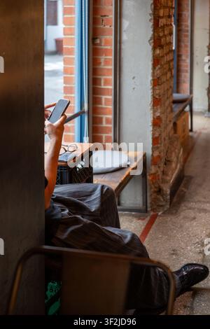 A customer relaxing in a quiet corner of an industrial-style coffee shop, focused on their smartphone. Stock Photo