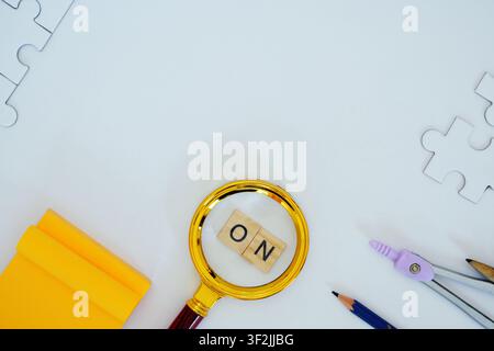 A magnifying glass focusing on wooden letters resting on white surface. Stock Photo