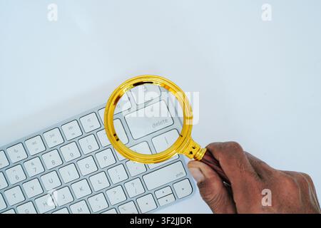 A hand holds a golden magnifying glass over the delete key. Stock Photo