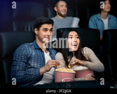 Beautiful young couple with popcorn watching movie in cinema Stock Photo