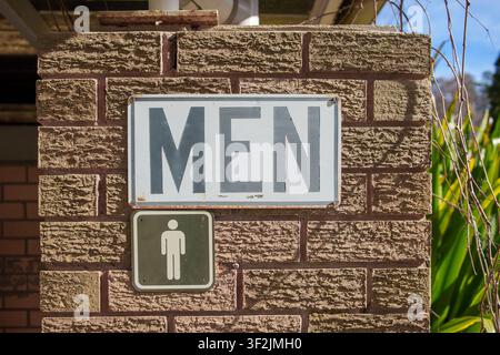 A clear directional sign for men's facilities mounted on a weathered brick wall, illuminated by natural outdoor daylight. Stock Photo