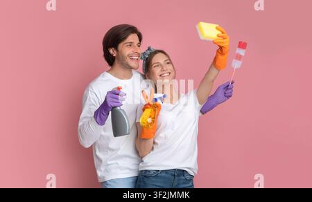 Cleaning Fun. Cheerful millennial couple taking selfie, using sponge like smartphone Stock Photo