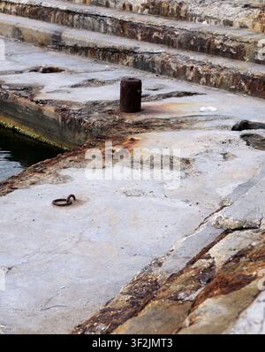 Concrete dock stairs and mooring bollard displaying heavy rust, erosion, and decay from prolonged exposure to water and elements. Bulgaria, varna, 16 Stock Photo