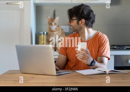 Young man using laptop at table with cute cat in home office Stock Photo