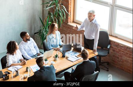 Employer Giving Speech On Meeting With Employees Sitting In Office Stock Photo