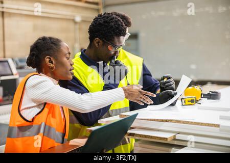 Factory workers collaborating on project blueprints at lumberyard Stock Photo