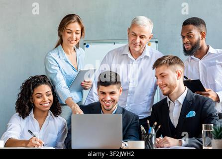 Smiling Coworkers Working Together On One Laptop In Modern Office Stock Photo