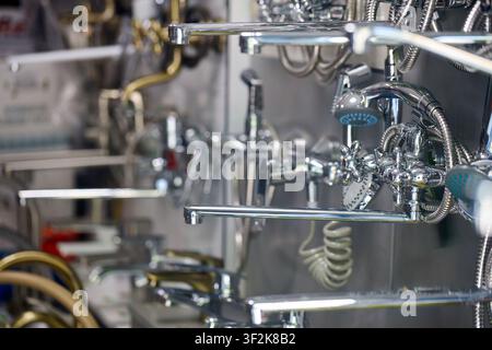 Selection of chrome and brass bathroom faucets, shower heads, long spouts, water taps, flexible hoses displayed on metal rack wall in plumbing store s Stock Photo