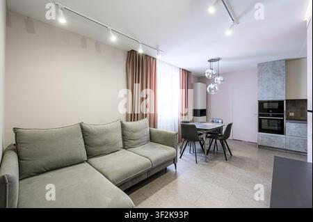 cozy living space with a gray sofa, dining table set, and kitchen area. Soft lighting and neutral tones create a welcoming atmosphere Stock Photo