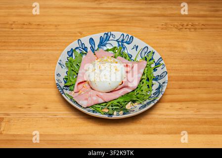 Creamy Burrata Cheese Nestled in Mortadella and Fresh Arugula on a Blue Floral Ceramic Plate Stock Photo