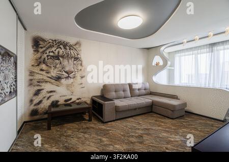modern living room features a large snow leopard mural, a gray sectional, and a uniquely shaped ceiling with recessed lighting Stock Photo
