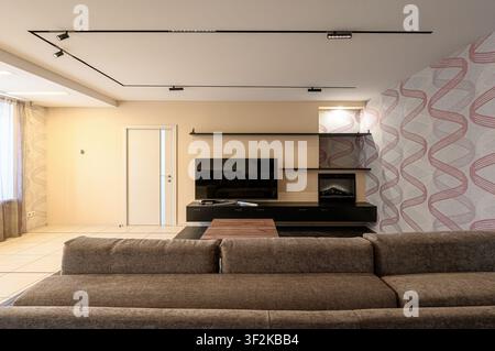 Modern living room featuring a large brown sofa, TV on a black console, and patterned wallpaper.  Track lighting adds contemporary flair Stock Photo