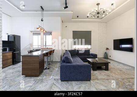 Modern apartment interior with blue sofa, kitchen island, sleek appliances, and stylish lighting Stock Photo