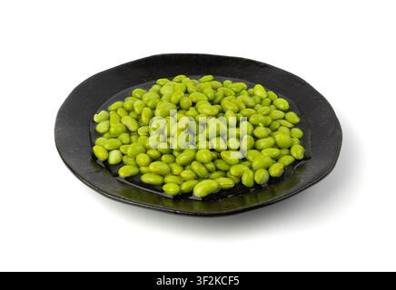 Edamame beans on black plate isolated. Green soy bean pile, cooked young soybean, boiled Japanese pea on white background Stock Photo