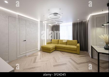 Bright living room with a yellow sofa, herringbone floor, ring-shaped lights, elegant wall décor, and grey curtains Stock Photo