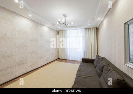 bright living room with patterned wallpaper, a soft beige rug, and a brown sofa. Natural light filters through sheer curtains by the window Stock Photo