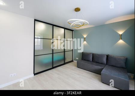 modern living room features a frosted glass partition, gray sectional sofa, and stylish gold lighting fixtures against mint green and white walls Stock Photo