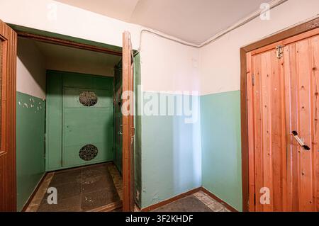 interior shows a hall with a green security door and an opened brown door. Walls are painted white and light green. A wooden door is on the right Stock Photo