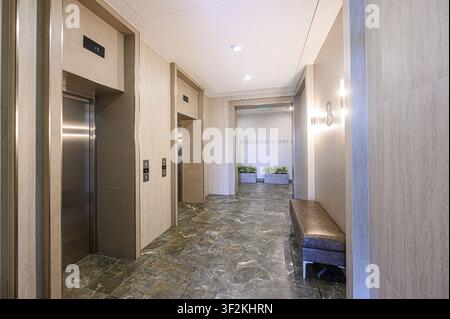 modern building hallway with two elevators, marble floors, a bench, and plants visible in the background Stock Photo