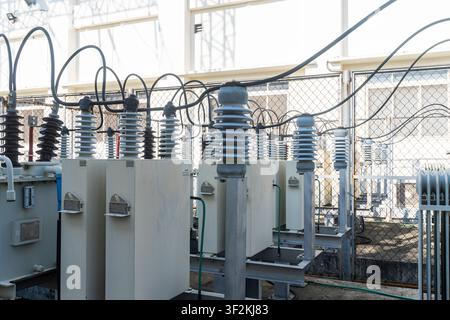 Close up of high voltage power transformers and ceramic insulators inside an electrical substation, showing cables, bushings, and power grid infrastru Stock Photo
