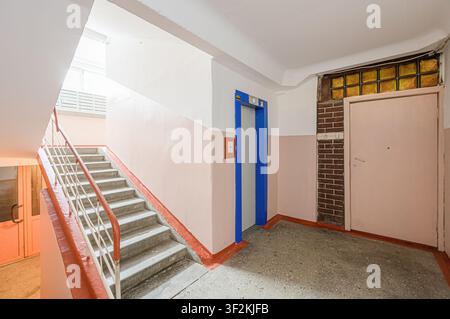 interior shot of a building hallway featuring stairs, an elevator, and a door. The walls are painted with a two-tone color scheme: white and light pin Stock Photo