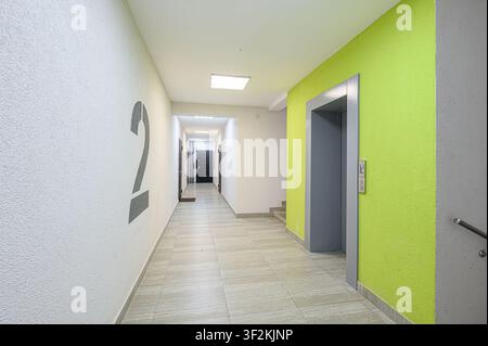 bright hallway with a large "2" on the wall, leading to doors. An elevator is on the right with a lime green wall accent Stock Photo