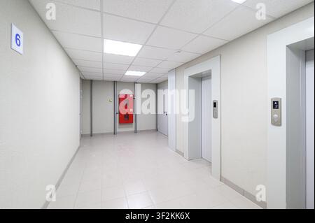 bright hallway featuring elevators, a fire hose cabinet, tiled floor and a number '6' sign on the wall Stock Photo