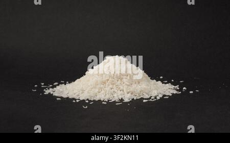 Grated coconut powder pile. Dry coco flakes pile, shredded desiccated coconut, tropical fruit chips texture, shaved nut on black background Stock Photo